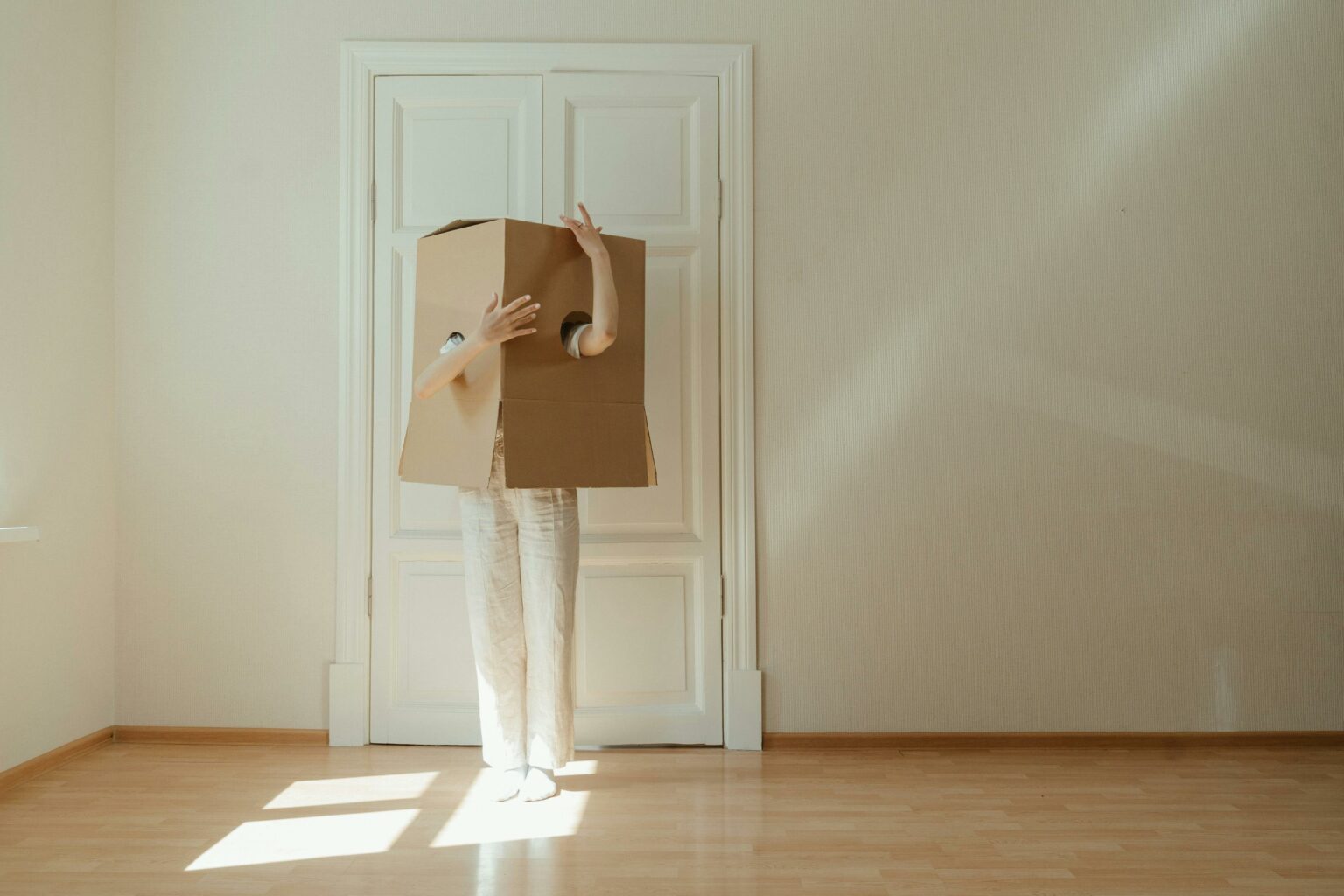 Woman in White Long Sleeve Shirt and White Pants Standing on Brown Wooden Floor