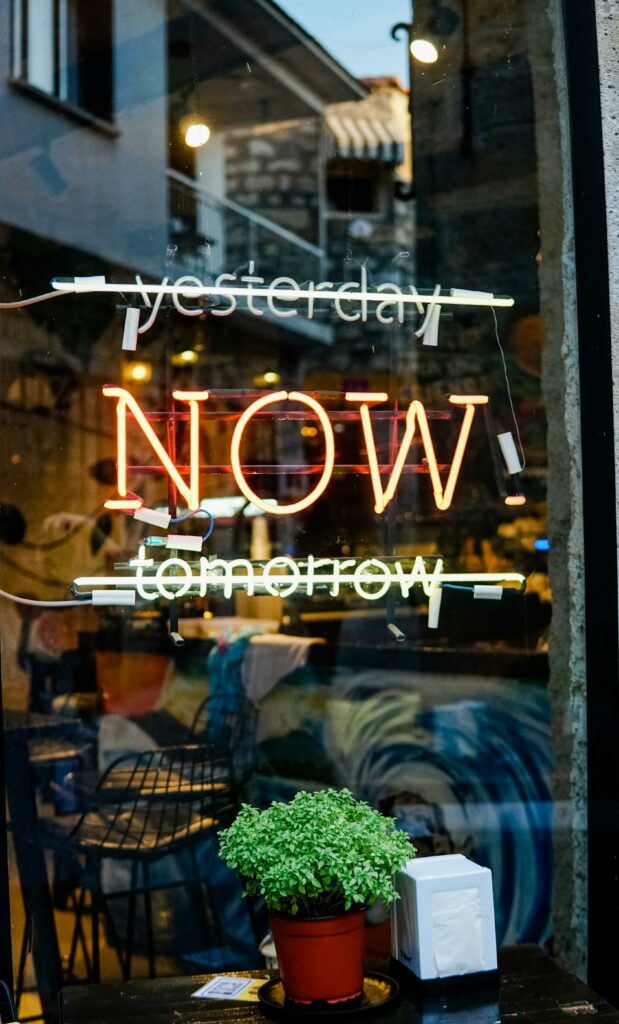pexels-photo-9226854-9226854 Colorful neon sign on a glass storefront with urban reflections and greenery.