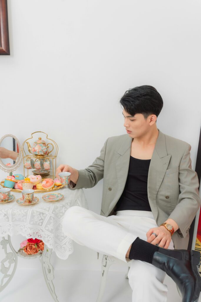 Sophisticated man in a blazer having tea with colorful pastries, seated indoors.
