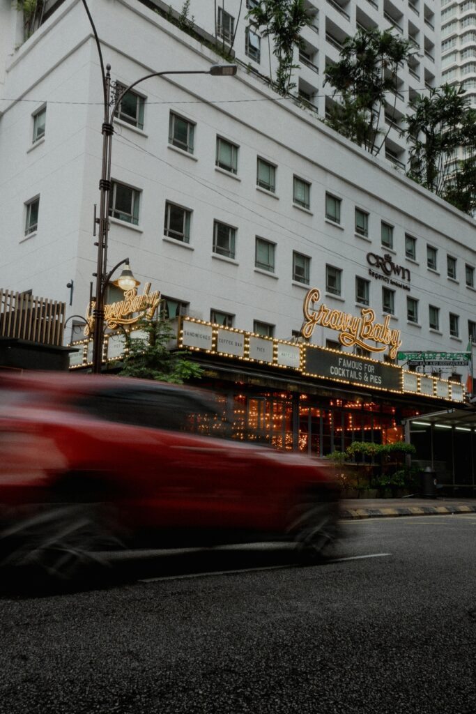 Blurred red car speeding past a lively urban city street with illuminated restaurant signs.
