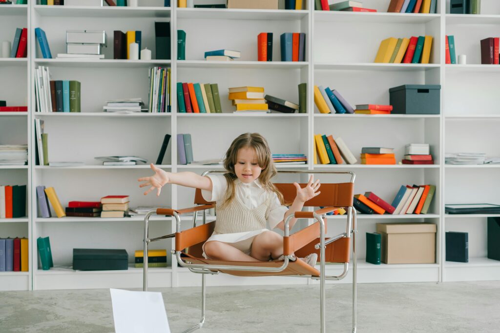 A young girl in a library sitting on a chair surrounded by colorful bookshelves.